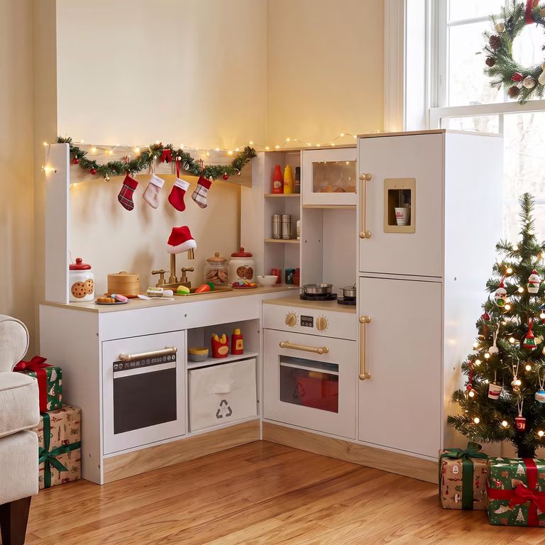 Christmas playroom decorating: white and gold play kitchen with garland, stockings, a mini Christmas tree and wrapped gifts