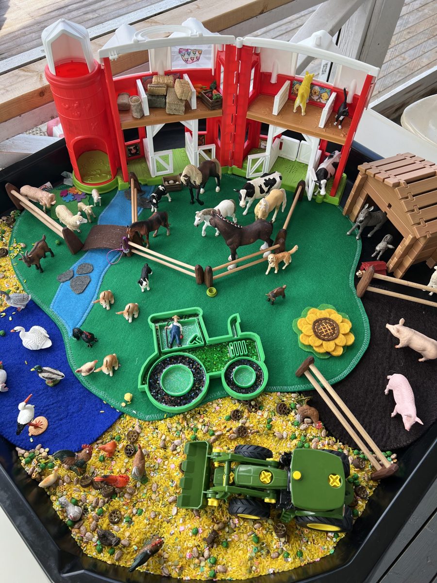 Farm small-world invitation to play with a red barn, horses, cows, pigs, a felt pond and a tractor in a sensory rice tray