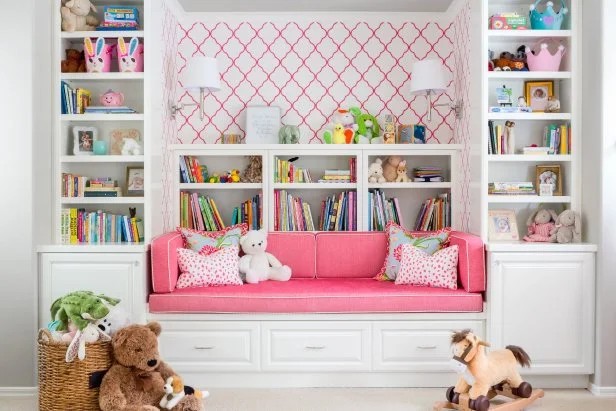 Pink girls playroom in Bethesda with a built-in window seat, pink cushion, white bookshelves, trellis wallpaper and stuffed animals