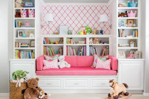 Pink window seat reading nook with white built-in bookshelves and trellis wallpaper